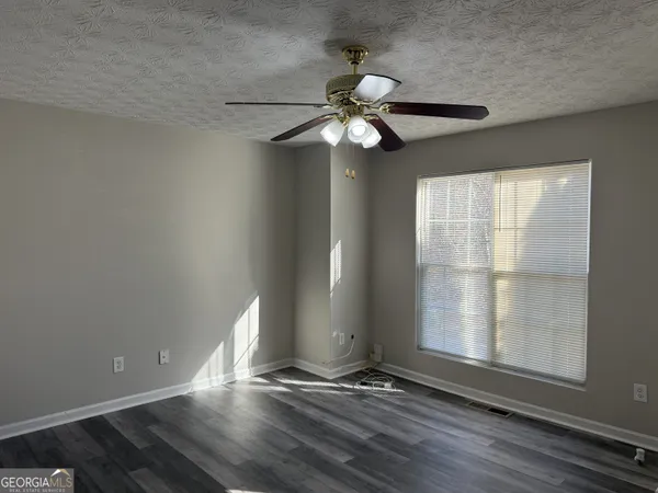 a view of an empty room with wooden floor and fan