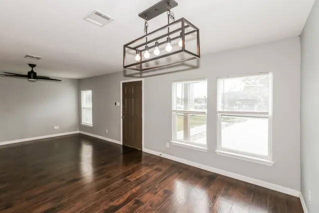 an empty room with wooden floor fan and windows