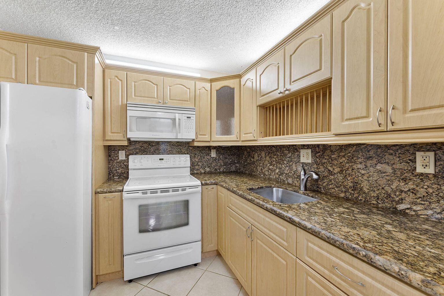 9440 Southwest 8th Street, Unit 318 Boca Raton, FL 33428 - Photo 2 of 11 a kitchen with granite countertop white cabinets and white appliances