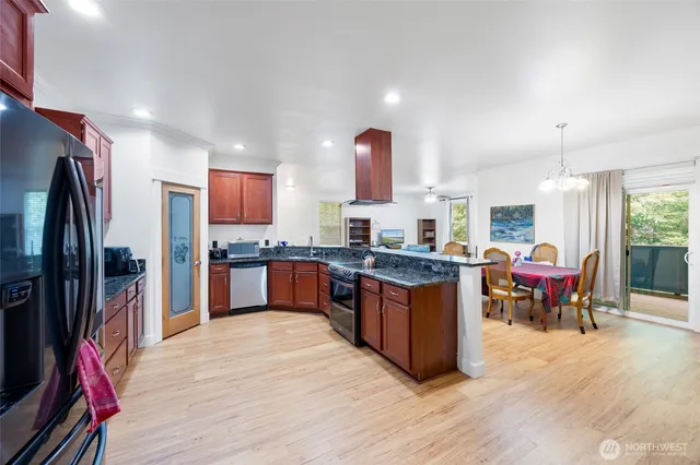 a kitchen with stainless steel appliances granite countertop a refrigerator a sink dishwasher a stove and a dining table with wooden floor