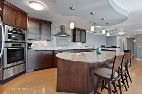 a kitchen with stainless steel appliances granite countertop a sink a stove a refrigerator cabinets and chairs