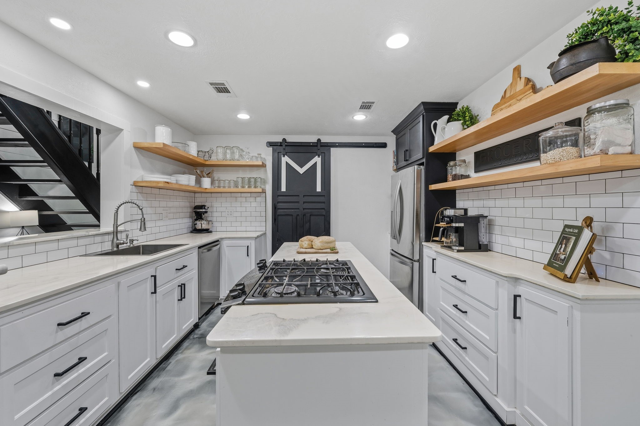 18 East Old Field Road Huffman, TX 77336 - Photo 10 of 35 This refined galley-style kitchen showcases an oversized island with gas range, abundant soft-close cabinetry, floating wood shelves, recessed lighting, & designer finishes that blend modern elegance with a farmhouse touch.
