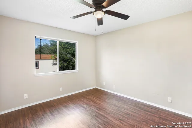 an empty room with wooden floor ceiling fan and window