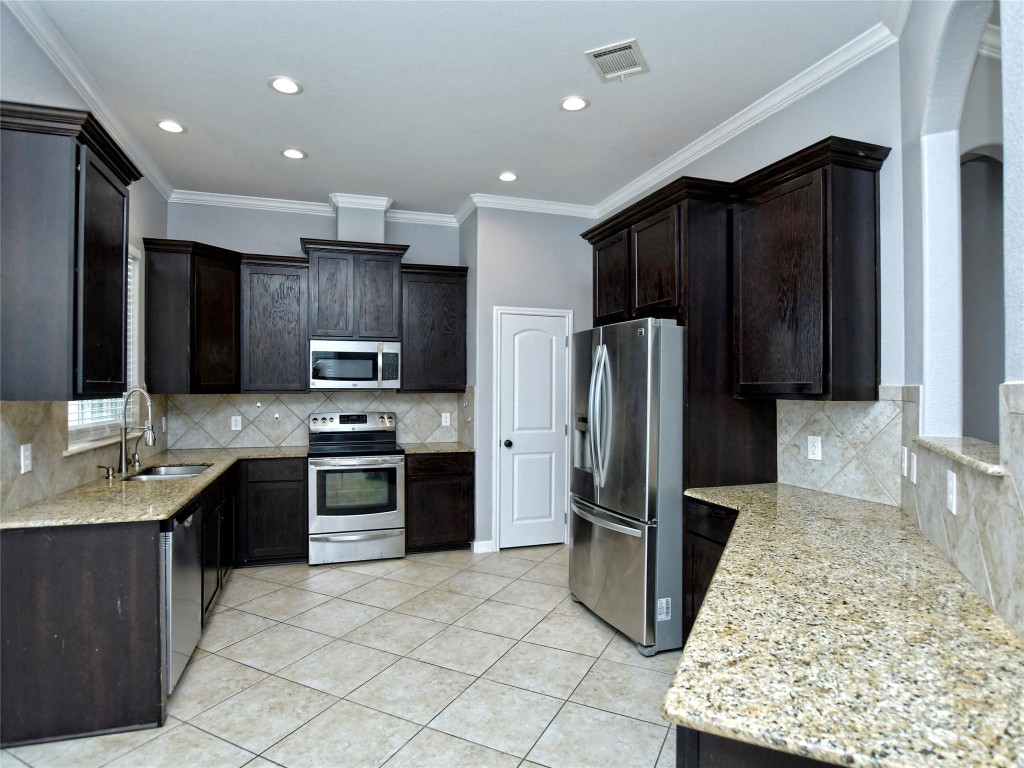 217 Geode Lane Jarrell, TX 76537 - Photo 10 of 35 Kitchen with stainless steel appliances, light stone countertops, light tile patterned flooring, ornamental molding, and dark brown cabinets
