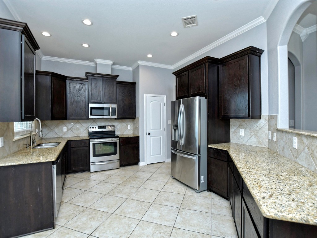 217 Geode Lane Jarrell, TX 76537 - Photo 15 of 35 Kitchen with stainless steel appliances, light stone counters, crown molding, light tile floors, and dark brown cabinets