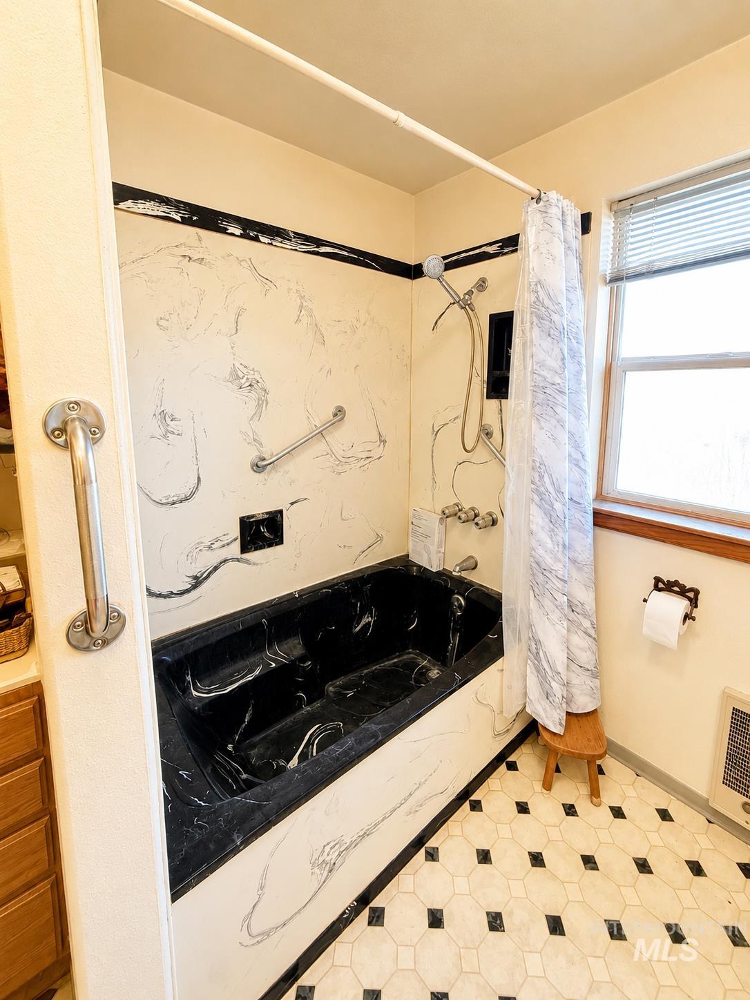 16434 Pride Lane Caldwell, ID 83607 - Photo 14 of 16 Bathroom featuring a black marble-look bathtub and shower surround, textured wall paneling, and hexagonal floor tiles with dark accents