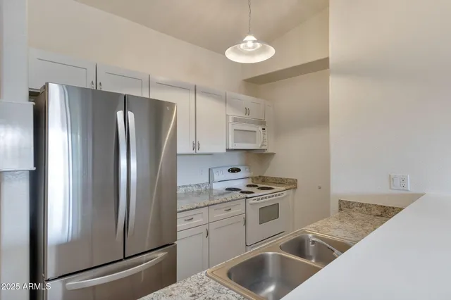 a kitchen with stainless steel appliances granite countertop a refrigerator a stove and a sink with wooden floors