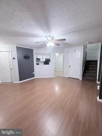 a view of an empty room with wooden floor and a ceiling fan