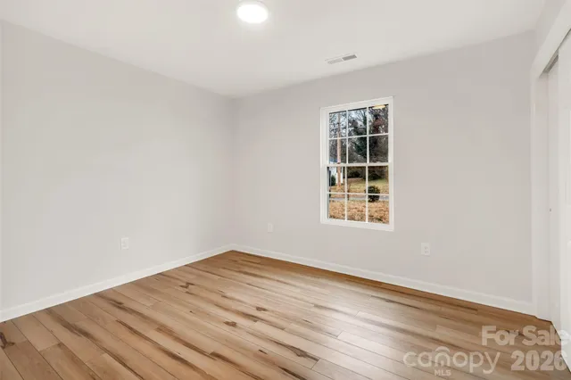 an empty room with wooden floor chandelier fan and windows