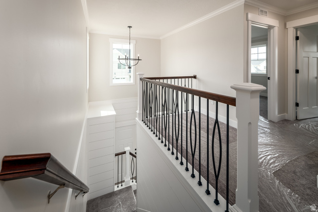 801 East Cys Road, Unit 19 Sandy, UT 84094 - Photo 6 of 11 Upper landing featuring a decorative wrought iron and wood-finish railing, a prominent window, a contemporary chandelier, crown molding, and a paneled wall detail along the staircase