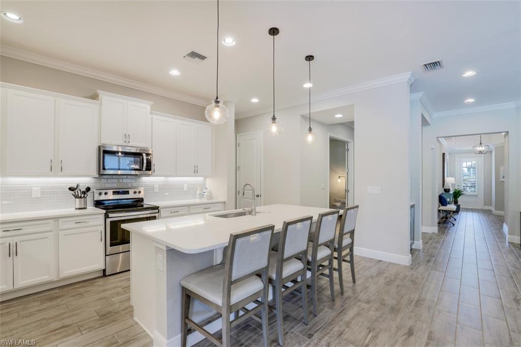 3528 Pilot Circle Naples, FL 34120 - Photo 15 of 46 a kitchen with stainless steel appliances granite countertop a stove a refrigerator a kitchen island a sink and white cabinets with wooden floor