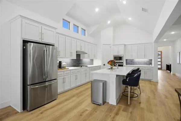 a kitchen with stainless steel appliances granite countertop a refrigerator a sink dishwasher a stove and white cabinets with wooden floor