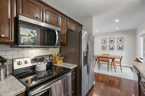 a kitchen with stainless steel appliances granite countertop a stove top oven a refrigerator a dining table and chairs with wooden floor