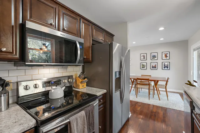 a kitchen with stainless steel appliances granite countertop a stove top oven a refrigerator a dining table and chairs with wooden floor