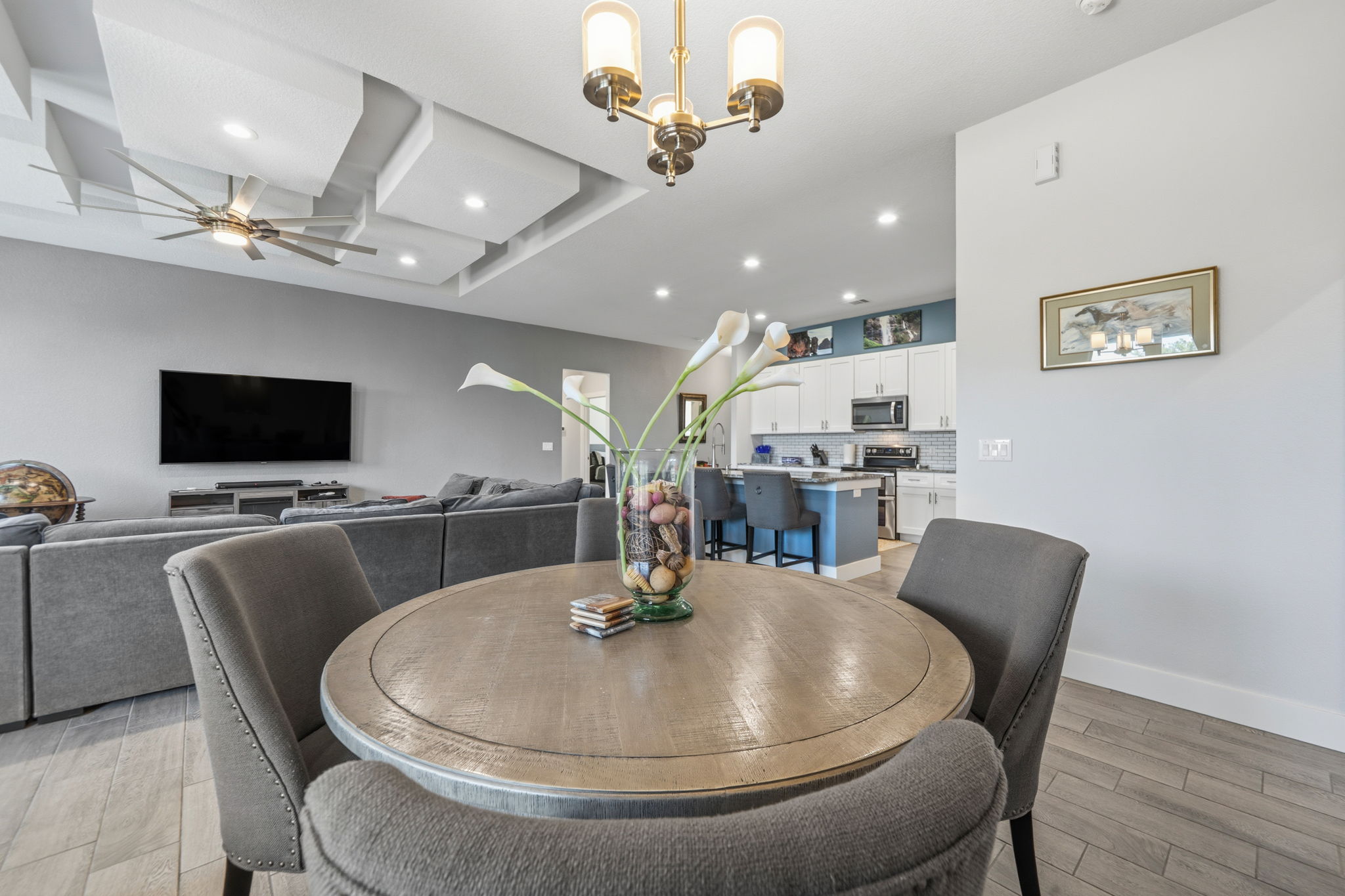 18605 Masters Cove Point Venture, TX 78645 - Photo 14 of 40 Bright living space featuring a tray ceiling with recessed lighting and a ceiling fan, wood-finish flooring, and a kitchen with white cabinetry and a blue island