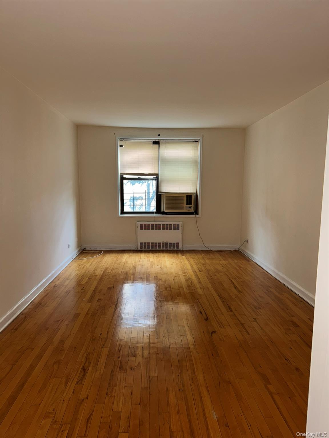 88-10 34th Avenue, Unit 2M Queens, NY 11372 - Photo 3 of 12 an empty room with wooden floor and windows