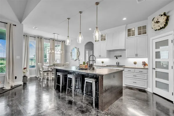 an open kitchen with granite countertop a stove a sink a dining table and chairs with wooden floor