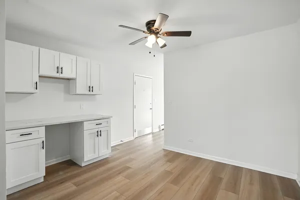 a view of an empty room with wooden floor and a ceiling fan
