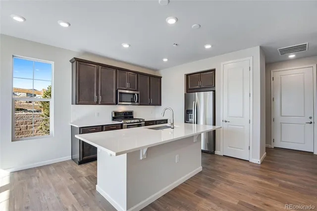 a kitchen with stainless steel appliances granite countertop a stove top oven a refrigerator a sink and a microwave with wooden floor