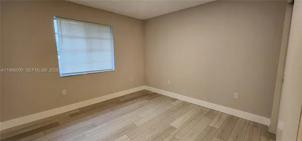 a view of an empty room with wooden floor and a window