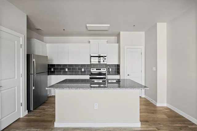a view of empty room with wooden floor and kitchen view