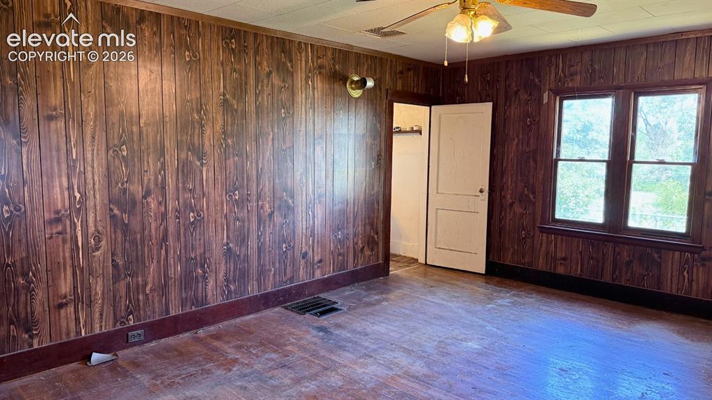 3380 Curtis Road Peyton, CO 80831 - Photo 8 of 13 Interior room featuring wood-panel walls, wood-finish flooring, a ceiling fan with integrated lighting, and a double-pane window