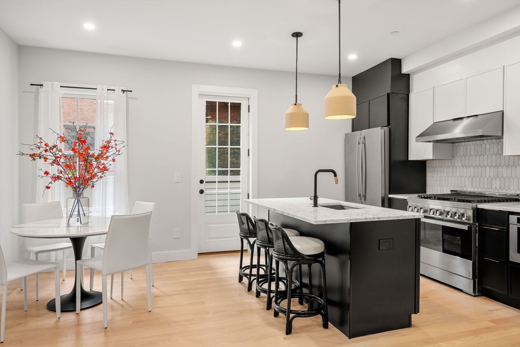 67 Revere Street, Unit 1 Boston, MA 02114 - Photo 2 of 29 a kitchen with stainless steel appliances granite countertop a stove a refrigerator a kitchen island a dining table and chairs with wooden floor