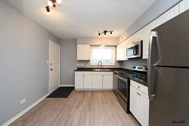 a kitchen with stainless steel appliances white cabinets a sink a stove a refrigerator and microwave