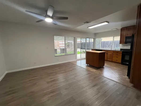 an empty room with wooden floor and kitchen view