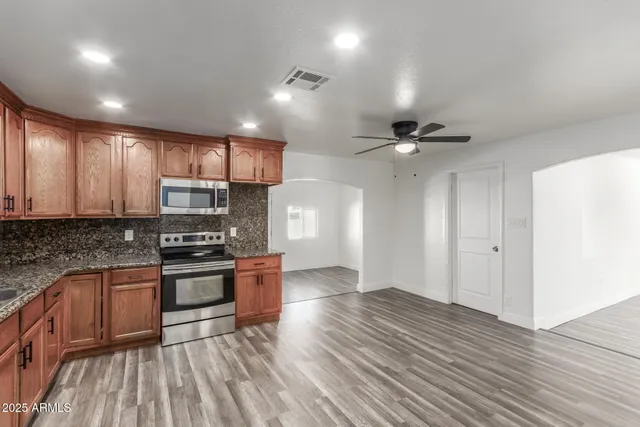 a kitchen with stainless steel appliances granite countertop a refrigerator a sink dishwasher a stove and white countertops with wooden floor