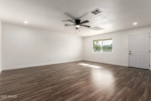 an empty room with wooden floor ceiling fan and windows