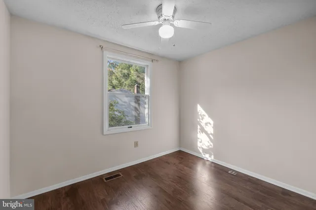 an empty room with wooden floor chandelier fan and windows
