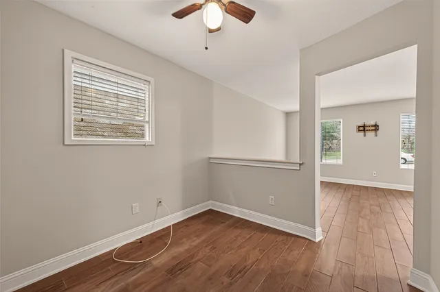 an empty room with wooden floor chandelier fan and windows
