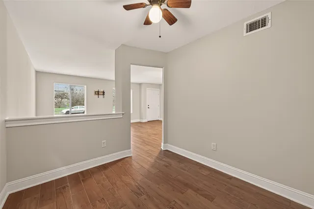 an empty room with wooden floor chandelier fan and windows