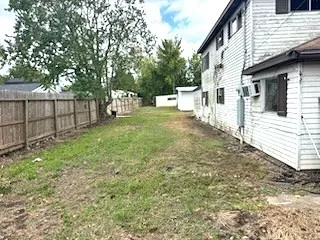 a view of a white house that has a small yard and large trees