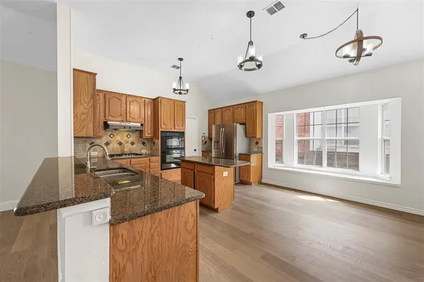 a kitchen with stainless steel appliances granite countertop a refrigerator a stove top oven a sink dishwasher and wooden cabinets with wooden floor