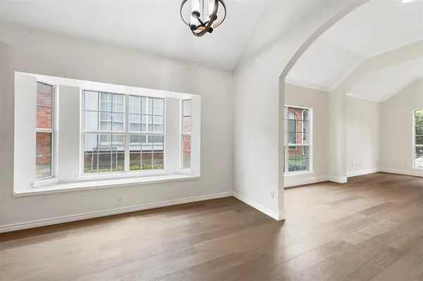 an empty room with wooden floor chandelier and windows