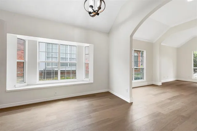 an empty room with wooden floor chandelier and windows