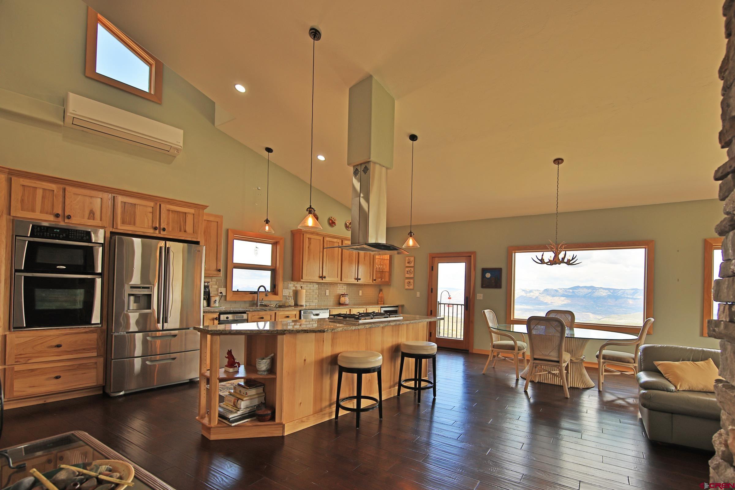 53315 Bull Basin Road Mesa, CO 81643 - Photo 13 of 44 a kitchen with stainless steel appliances kitchen island granite countertop a stove a refrigerator a dining table and chairs with wooden floor
