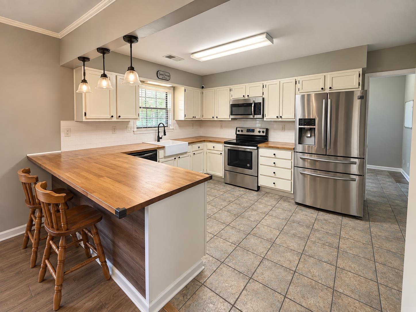 3771 West Union Road Millington, TN 38053 - Photo 5 of 16 U-shaped wood-finish countertop with seating, stainless steel appliances, white cabinetry, farmhouse sink, and tile flooring