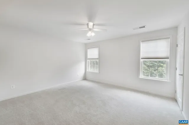 an empty room with chandelier fan and windows