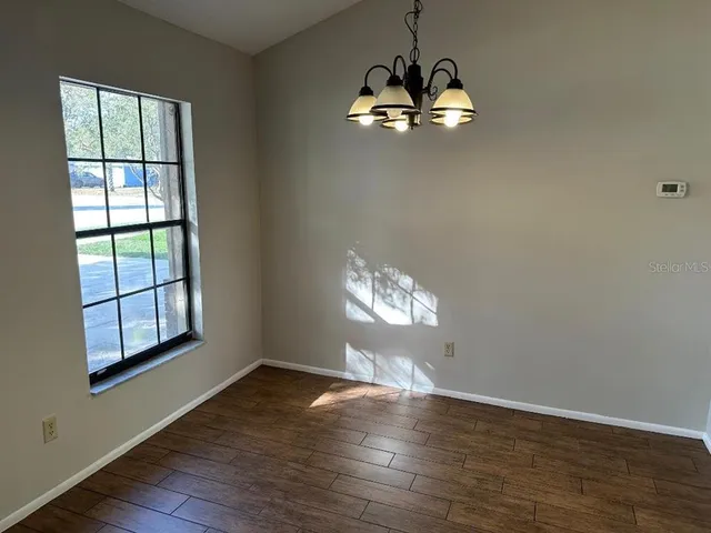 an empty room with wooden floor chandelier and windows
