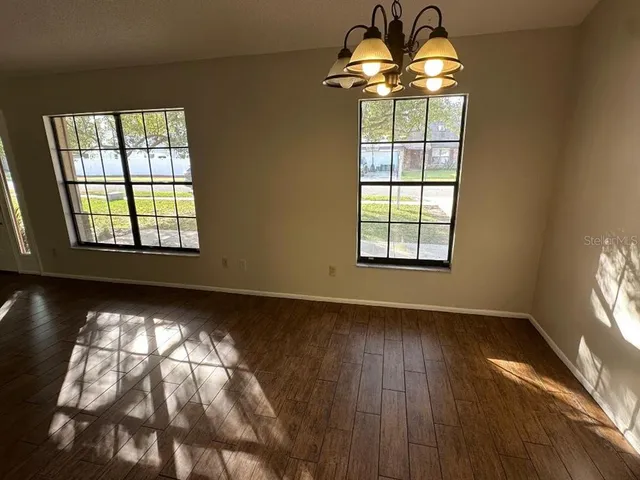 an empty room with wooden floor chandelier and windows