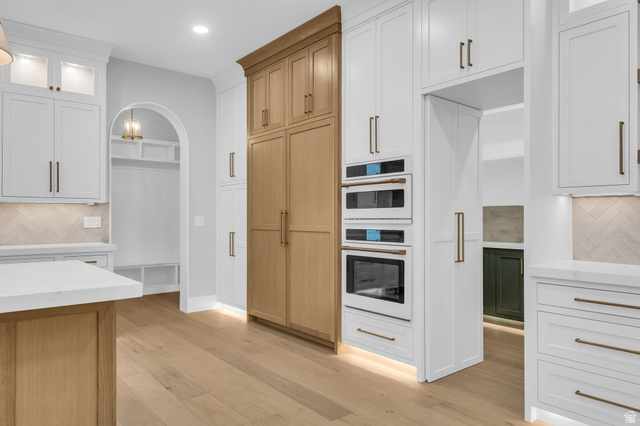 2828 Jojo Road Eagle Mountain, UT 84005 - Photo 12 of 63 Gourmet kitchen featuring a built-in oven and microwave, custom cabinetry with brass hardware, wood-finish flooring, a herringbone pattern tile backsplash, and a white countertop