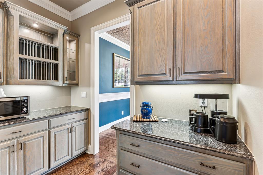 1815 West Forest Grove Road Lucas, TX 75002 - Photo 18 of 40 Kitchen featuring ornamental molding, dark stone countertops, stainless steel microwave, glass insert cabinets, and dark wood-style flooring