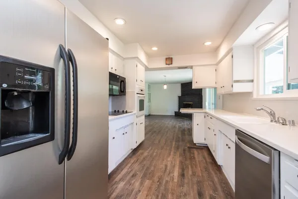 a large kitchen with stainless steel appliances kitchen island granite countertop a refrigerator oven a sink dishwasher and white cabinets with wooden floor