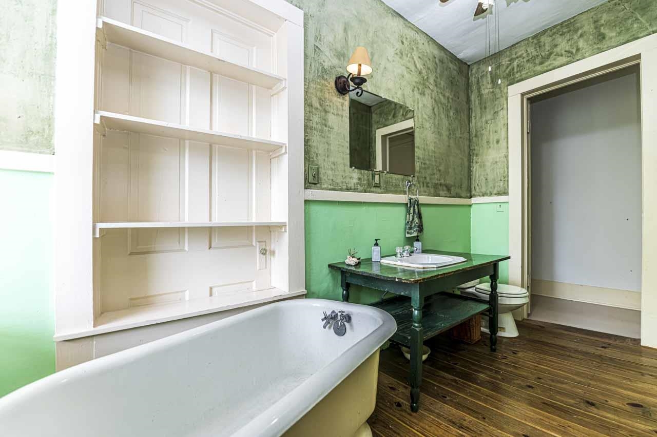 726 South Main Street Covington, TN 38019 - Photo 23 of 40 Freestanding bathtub with integrated wall shelving, wood-finish flooring, pedestal sink with open vanity, and wall-mounted sconce lighting