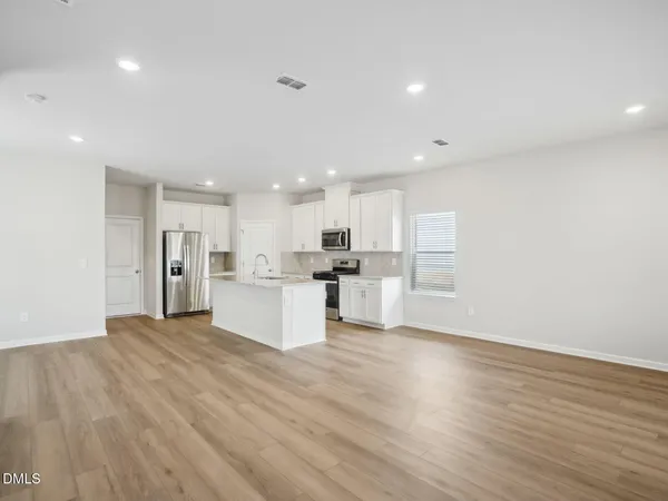 a kitchen with stainless steel appliances granite countertop a refrigerator oven a sink dishwasher and white cabinets with wooden floor