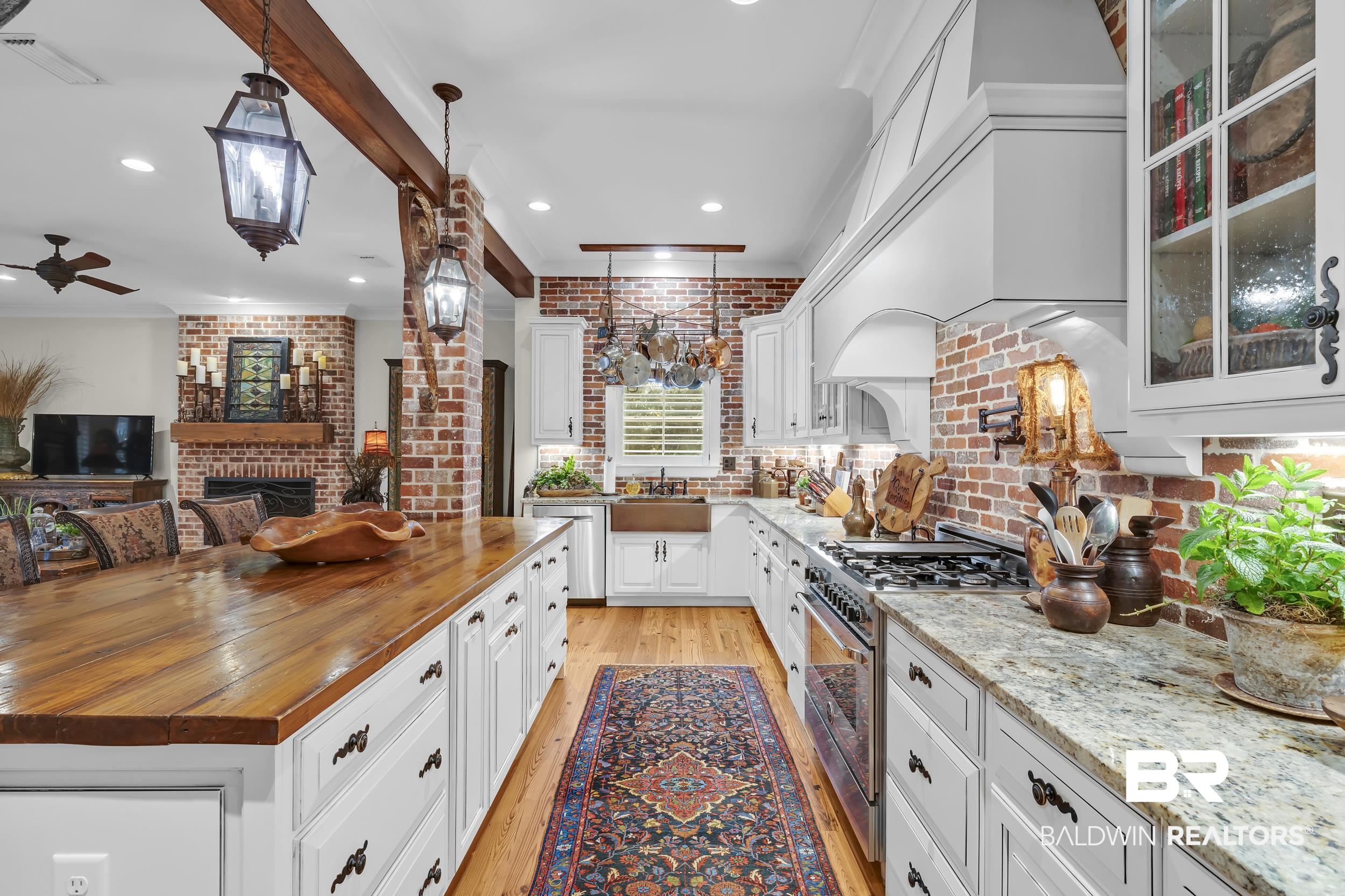 12161 Jessamine Street Magnolia Springs, AL 36555 - Photo 19 of 70 Kitchen featuring a brick fireplace, white cabinets, stainless steel appliances, light wood finished floors, and hanging light fixtures