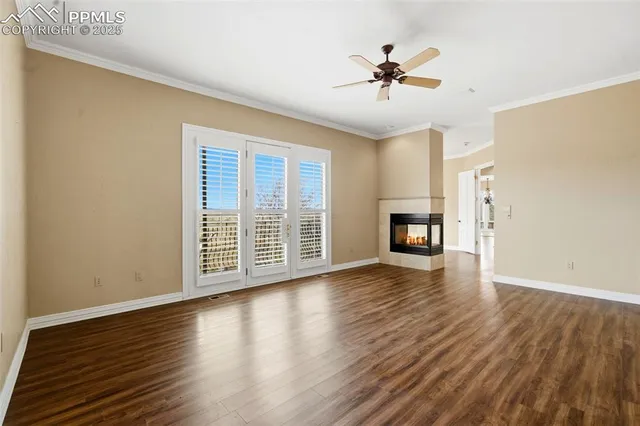 a view of an empty room with wooden floor and a ceiling fan